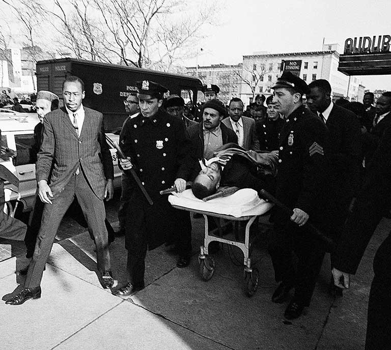 Malcolm X is taken away from the Audubon Ballroom on a stretcher after being shot.