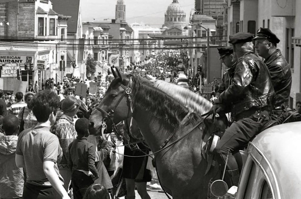 Mounted policemen watch a Vietnam War protest march in San Francisco, as thousands of marchers stream by (1967)