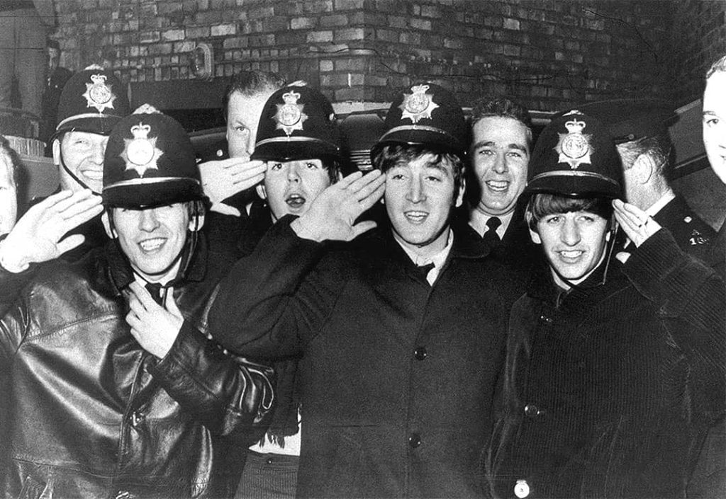 John Lennon (centre) with the rest of the Beatles posing with Birmingham police offices whilst wearing their 'bobbies' hats (1963)
